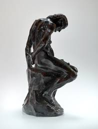 La sculpture est noire et brillante. Une vielle femme se tient assise et recroquevillée, les mains dans le dos. Ses os paraissent à travers sa peau.