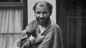 Klimt regarde le photographe avec bonhomie. Il tient dans ses bras un chat qui regarde également le photographe. Le peintre a le front dégarni, il porte un ample tablier.