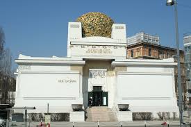Sur la photo on voit le palais de la Secession. Ce bâtiment est très clair et fait de formes rectangulaires, mis à part la grande sphère sur le toit qui est faite de fleuilles dorées.